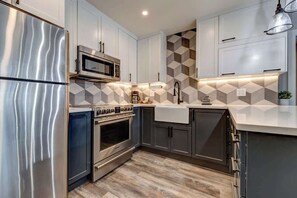 A modern kitchen with stainless steel appliances, a microwave, and a patterned backsplash. - Greystone Lodge 329 Ski-in/Out by Acer Vacations (Whistler)
