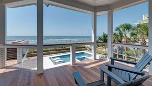 Uma área externa coberta com piscina, espreguiçadeiras e vista para o oceano.