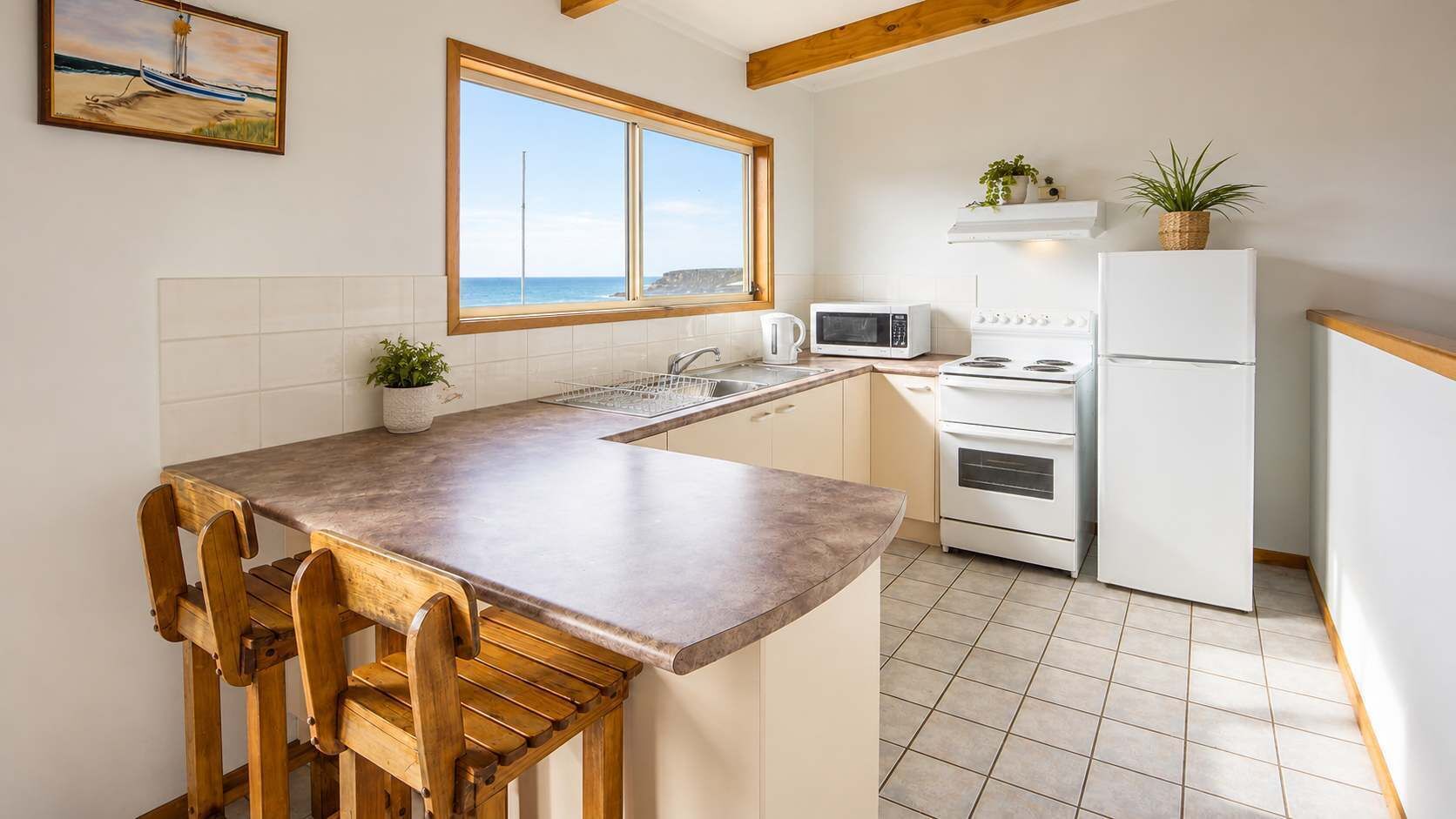 Una cocina con isla de madera, electrodomésticos blancos y vistas al mar a través de una ventana.