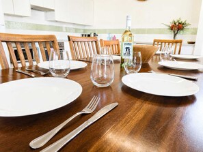 Une table à manger dressée avec de l’assiette blanche, des couverts et des verres transparents, et une bouteille de vin SILOS posée sur la table.
