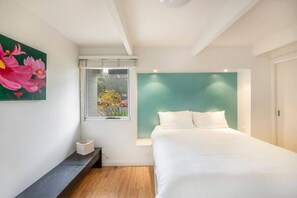 Ein Schlafzimmer mit Bett, einem Fenster mit Blick auf Blumen und einem Bild an der Wand.