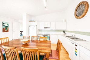 A modern kitchen with white cabinets, a wooden dining table, and a wall-mounted clock.