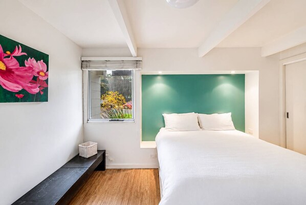 A bedroom with a bed, a window with a view of flowers, a green accent wall, and a white ceiling.