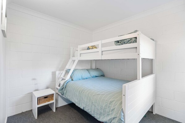 Una cama individual sobre otra con una escalera, una mesita de noche pequeña y una cesta.