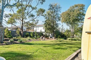 Ein gepflegter Garten mit Rasen, einer Holzdiele und verschiedenen Bäumen.