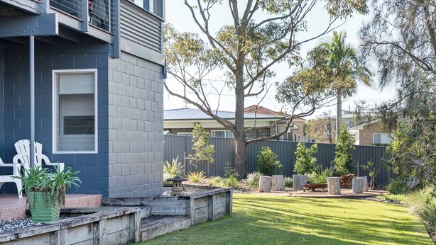 A residential backyard with a lawn, a wooden deck, and a variety of plants. - Retro Beach House at Mollymook (Mollymook)