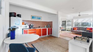 A modern kitchen with red cabinets, a white dining table, and blue chairs. - Retro Beach House at Mollymook (Mollymook)