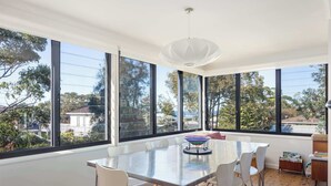 Un espace repas moderne avec une table en verre, des chaises blanches et de grandes fenêtres donnant sur l’extérieur.