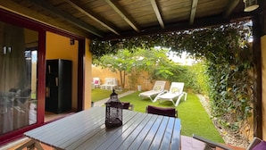 Un patio con tavolo e sedie, un lanterna e vista su un giardino con poltrone relax e prato.