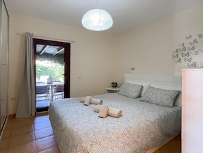 A bedroom with a bed, a nightstand, a wall-mounted light fixture, and a view through a door.