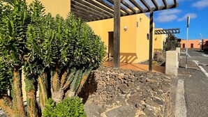 Un edificio con facciata gialla, un pergolato in legno e piante di cactus.