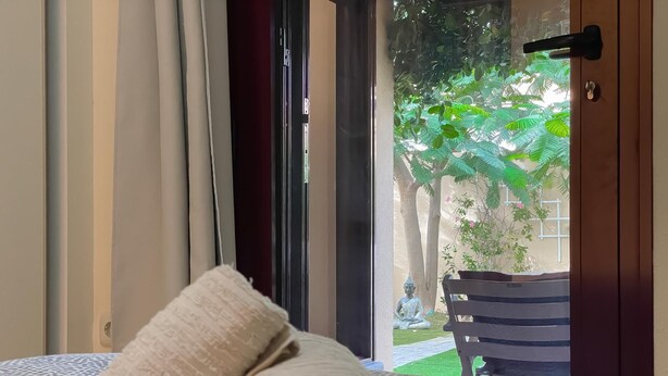 Un letto rifatto con cura, un asciugamano arrotolato, vista su un giardino con una statua e una porta in legno.