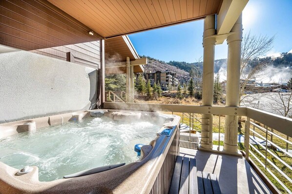 A hot tub on a wooden deck with a view of a mountainous landscape.