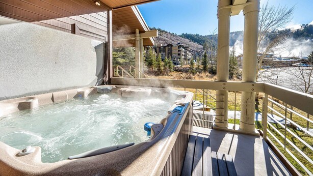 A hot tub on a wooden deck with a view of a mountain resort.