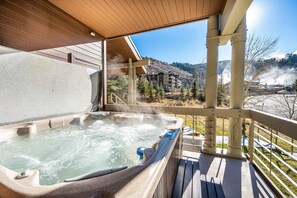 A hot tub on a wooden deck with a view of a mountain resort.