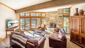 A spacious living room with a stone fireplace, large windows, and a cozy seating area.