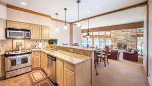 A spacious kitchen with granite countertops, wooden cabinets, and a stone fireplace in the dining area.