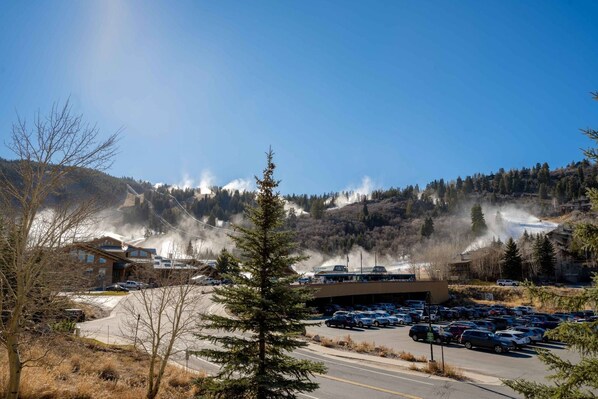 A parking lot with several cars, a building with a sloped roof, and a mountainous background with smoke or steam rising.