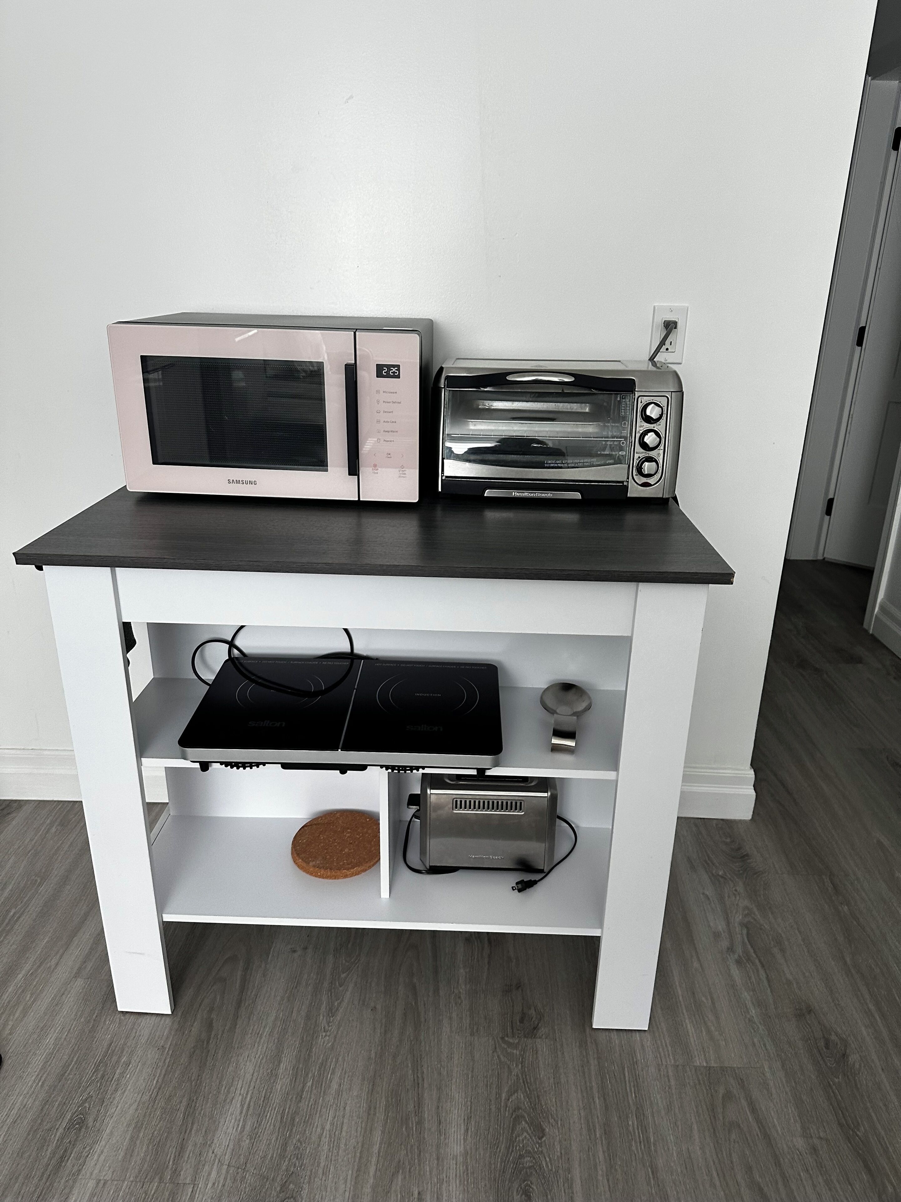 A kitchenette with a microwave, toaster, induction cooktop, and a small appliance on a white cabinet.