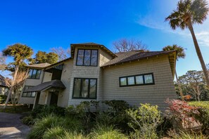 A two-story house with a sloped roof, large windows, and a well-maintained garden with various plants and a palm tree.