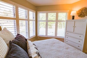 A bedroom with a large bed, white wicker furniture, and a view through the window.