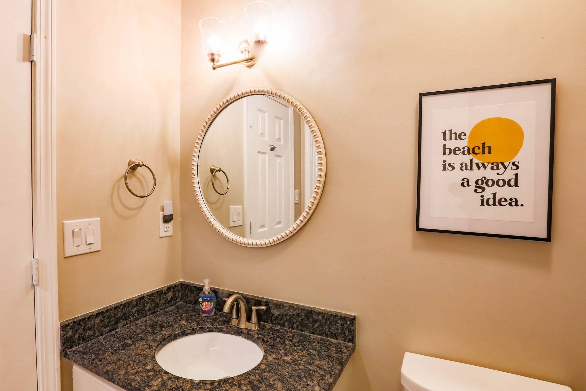 A bathroom with a round mirror, a sink, a toilet, and a framed quote on the wall.