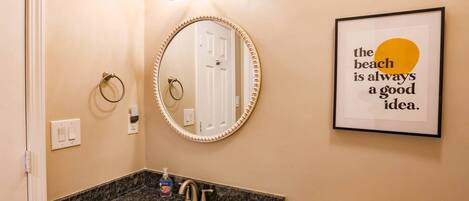 A bathroom with a round mirror, a sink, a toilet, and a framed quote on the wall.