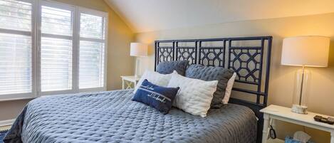 A neatly made bed with a grey quilt, a headboard with a geometric pattern, bedside lamps, and a small bedside table with a tissue box.