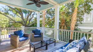 A covered porch with wicker furniture, a ceiling fan, and a view of surrounding trees. - 3 Min Walk to Beach! Serene Retreat w/ Heatable Private Pool, Ping Pong Table, Multiple Decks & Dens (Isle of Palms)