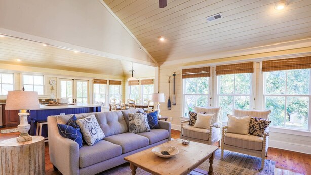 A spacious living room with a large sofa, a coffee table, and a dining area with a table and chairs. - 3 Min Walk to Beach! Serene Retreat w/ Heatable Private Pool, Ping Pong Table, Multiple Decks & Dens (Isle of Palms)