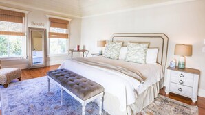 A bedroom with a large bed, a bench, a nightstand, and a mirror. - 3 Min Walk to Beach! Serene Retreat w/ Heatable Private Pool, Ping Pong Table, Multiple Decks & Dens (Isle of Palms)