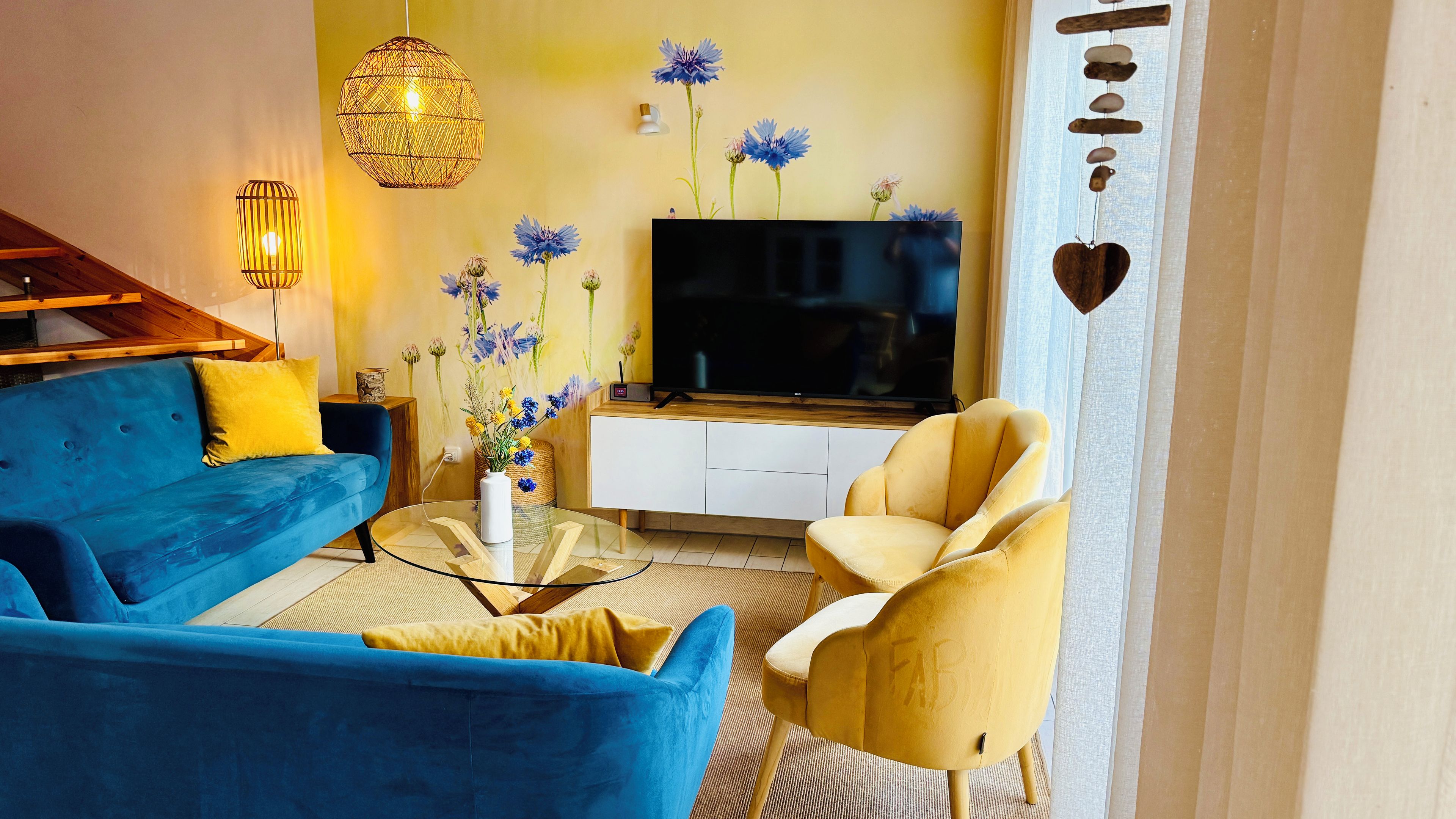 Ein Wohnzimmer mit blauem Sofa, gelbem Sessel und einem Flachbildfernseher auf einem weißen Schrank.