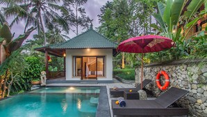 A pool area with lounge chairs, a small pavilion, and a stone wall. - D'Junas Villas by GenuineHost  (Ubud)