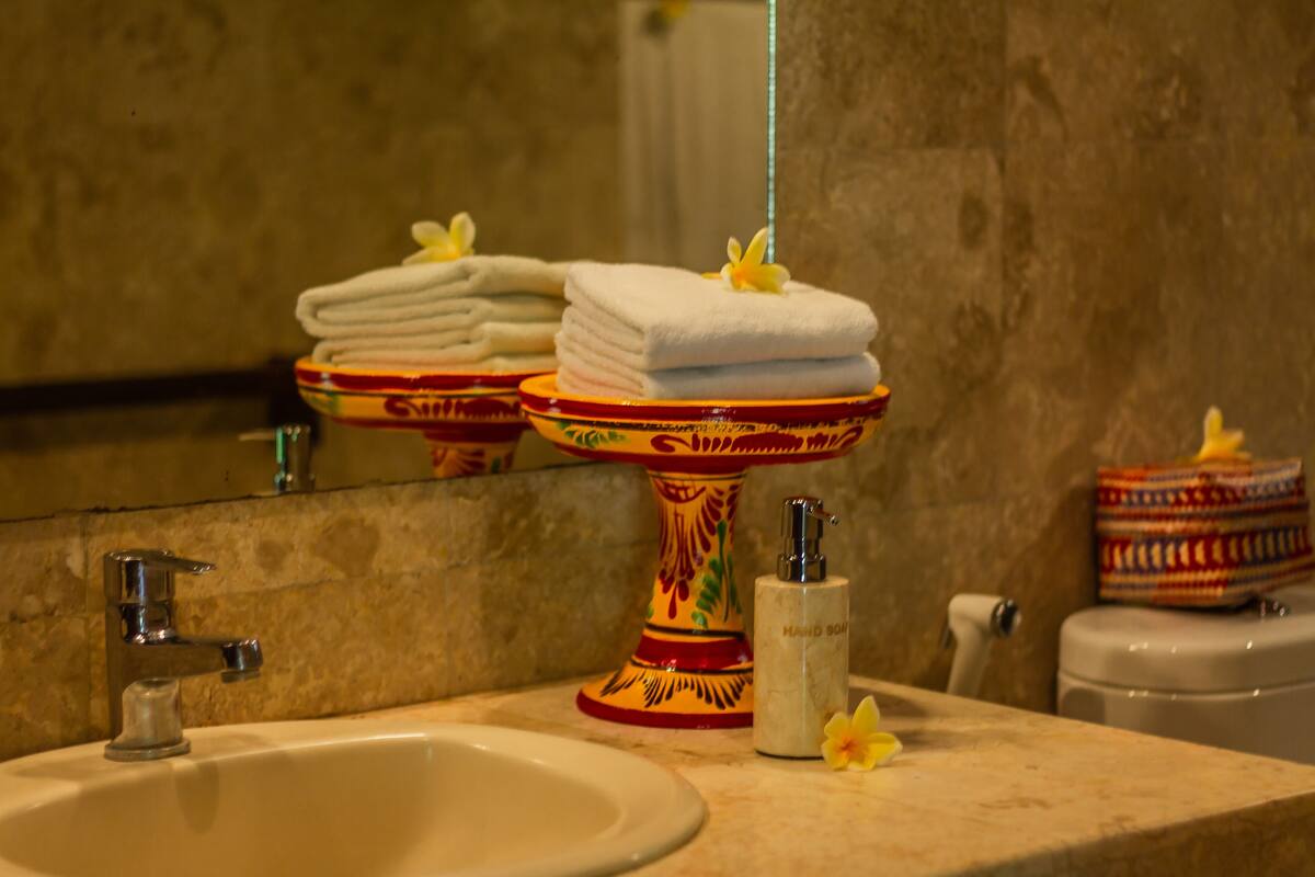 Une salle de bain comprenant un lavabo, un présentoir décoratif avec des serviettes, un distributeur de savon liquide et des toilettes.
