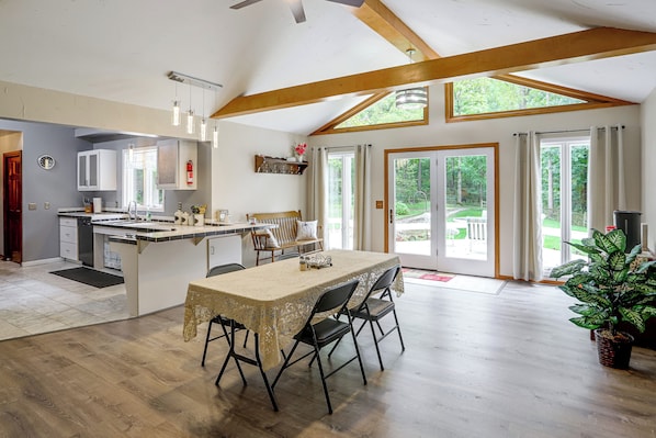 A spacious kitchen with a dining area, wooden beams, and a large sliding glass door leading to a garden. - Nature Lover's Cottage on Wooded Acreage (Nova)