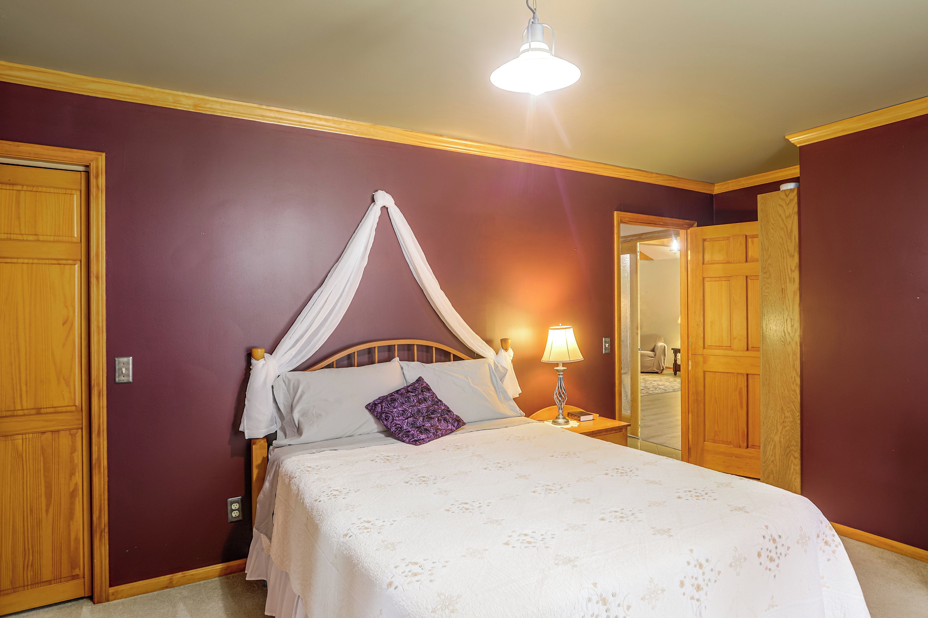 A bedroom with a canopy bed, a bedside lamp, and a door leading to another room.