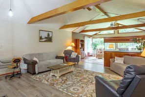 A spacious living room with a high ceiling, wooden beams, a fireplace, and a view of the outdoors.