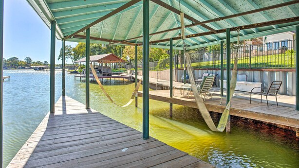 Un muelle cubierto que se extiende sobre el agua, con una estructura tipo pabellón, bancos de madera y un columpio.