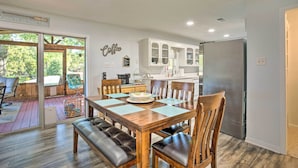 Un comedor con una mesa y sillas de madera, un banco y una cocina al fondo.