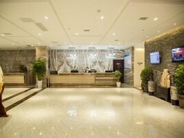 Zona de recepción de un hotel con suelo de mármol, mostrador de recepción y televisor empotrado en la pared.