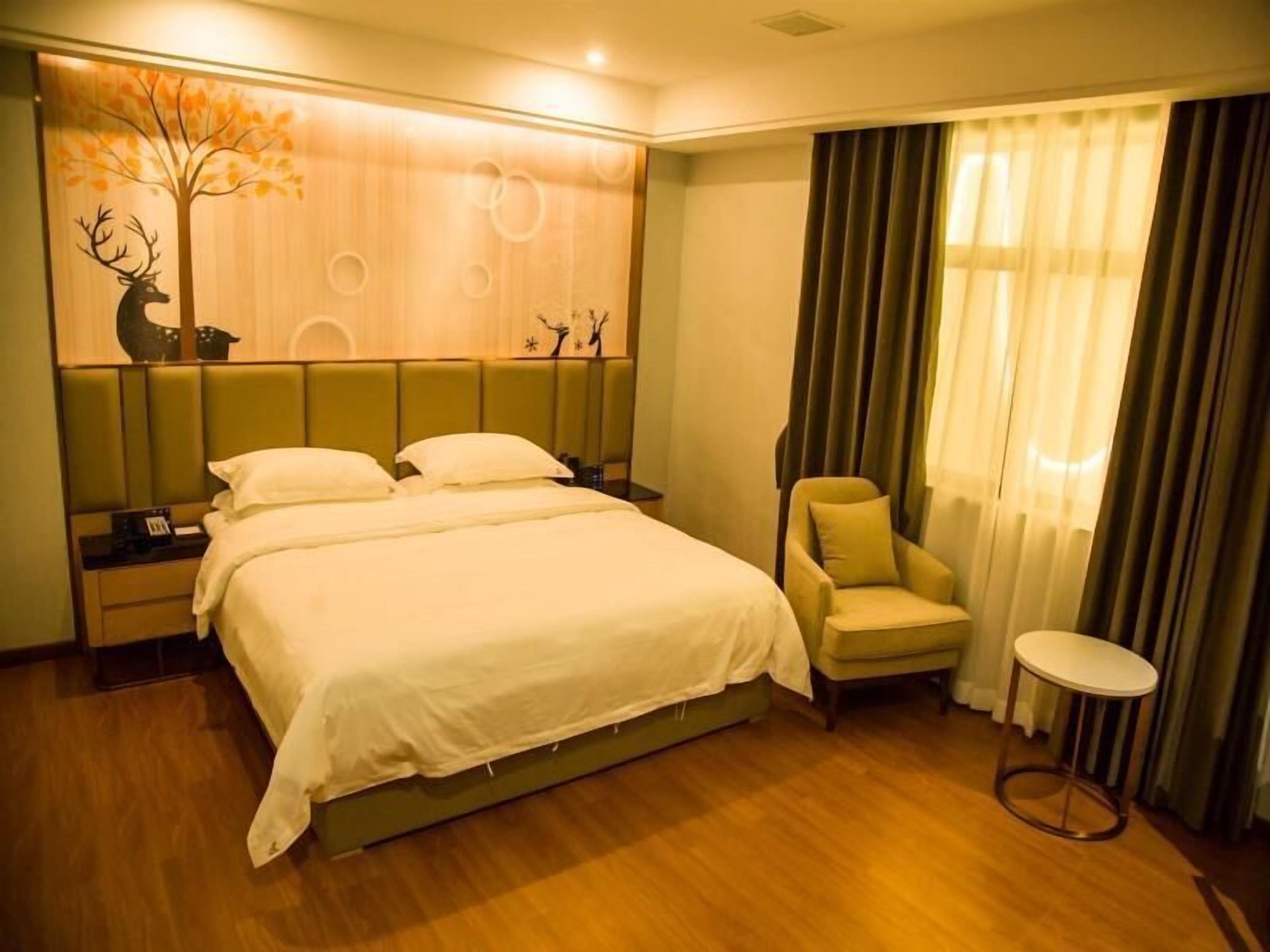 A hotel room with a large bed, a chair, a small table, and a decorative wall with a tree and animal silhouettes.