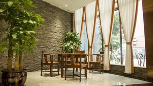 A lobby with a stone wall, a wooden table with chairs, and large windows with curtains. - Greentree Eastern Anshun Town Huangguoshu Avenue Jinhui Xindu Hotel (Anshun)