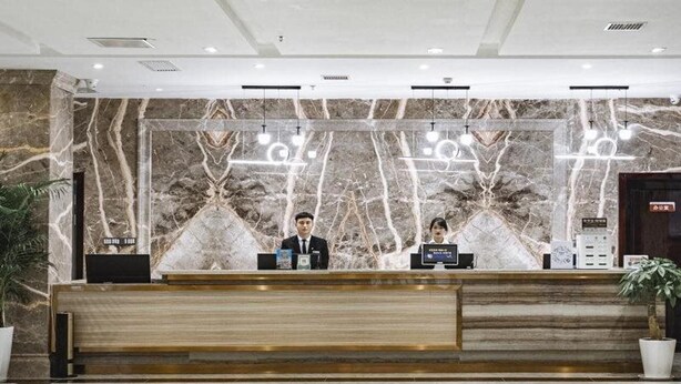 A reception desk with marble backdrops, two staff members, and a modern interior design. - Greentree Eastern Anshun Town Huangguoshu Avenue Jinhui Xindu Hotel (Anshun)