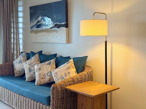 A wicker sofa with cushions, a small wooden table, a floor lamp, and a painting on the wall. - PLAGE BLEUE BEACHFRONT APARTMENTS BY LOV (Pointe Aux Piments)