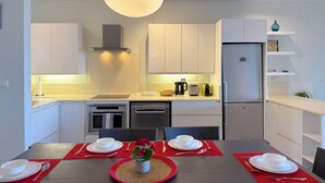 Una cocina moderna con gabinetes blancos, horno empotrado, lavavajillas y refrigerador.