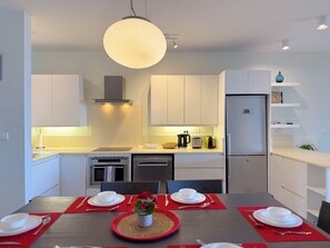 A modern kitchen with white cabinets, a built-in oven, a dishwasher, and a refrigerator. - PLAGE BLEUE BEACHFRONT APARTMENTS BY LOV (Pointe Aux Piments)