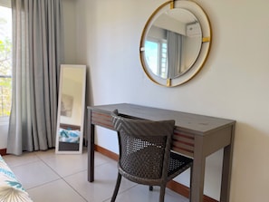 Ein Zimmer mit Schreibtisch, Stuhl, Spiegel und einem Fenster mit Vorhängen.