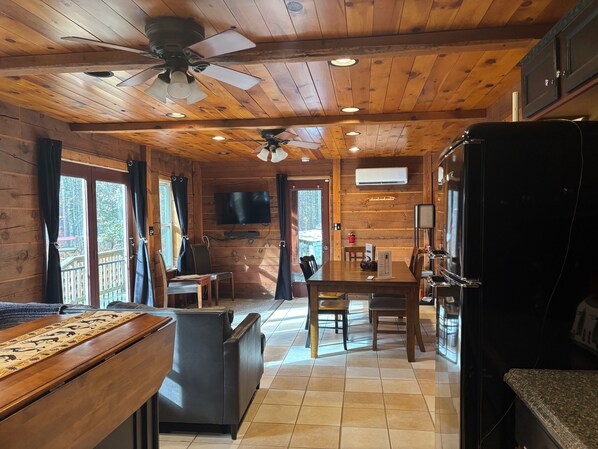 A wooden cabin interior with a dining area, kitchen, and a ceiling fan.