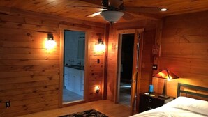 Un dormitorio de cabaña de madera con cama, mesita de noche, lámpara y ventilador de techo.