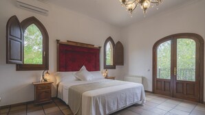 Une chambre à coucher avec un grand lit, deux tables de chevet, une tête de lit rouge et deux fenêtres en arc de cercle.